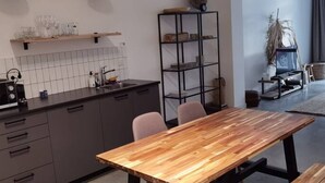 A modern kitchen with a wooden dining table, two pendant lights, and a built-in bookshelf.