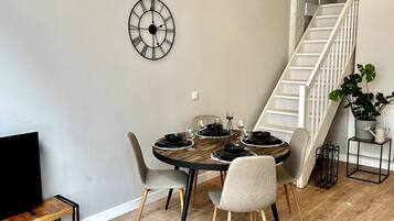 A dining area with a round table, four chairs, a wall clock, and a staircase.