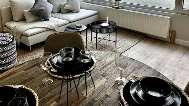 Ein modernes Wohnzimmer mit einer Couch, einem kleinen runden Tisch und Blick auf eine Straße durch ein großes Fenster.