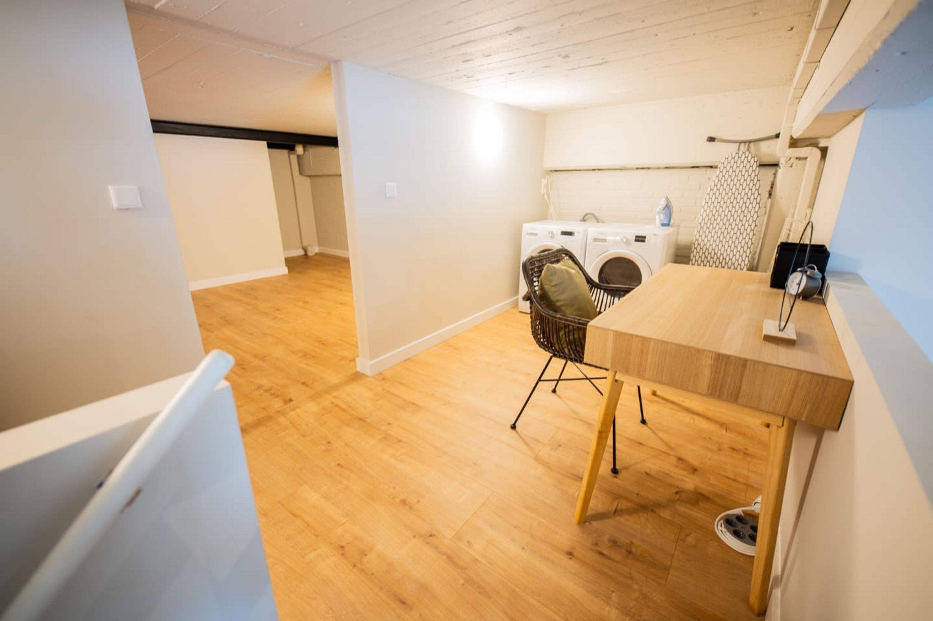 Una habitación pequeña con piso de madera, una mesita con una silla, una lavadora y un tendedero.