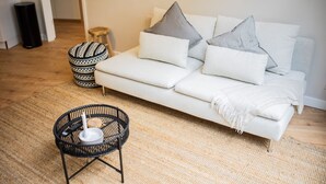 Ein modernes Wohnzimmer mit einem weißen Sofa, einem gemusterten Ottomanen und einem schwarzen Webstuhl-Sessel.