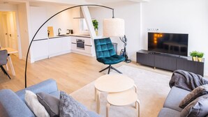 A modern living room with a sofa, a coffee table, and a TV. There is a kitchen in the background with white cabinets and a black countertop. - Nb306 Serviced Apartment 2,5br (Rotterdam)