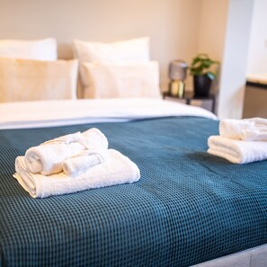 A neatly made bed with a teal bedspread and two folded white towels on the side.