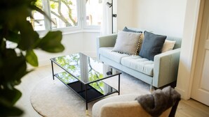 A living room with a light blue sofa, a glass coffee table, and a round rug. - Alphabet 1BR Serviced Apartment -nb304/306- (Rotterdam)