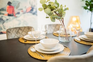 A dining table set with white plates, bowls, and wine glasses, with a vase of green leaves in the center.