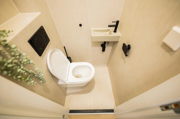 A compact bathroom with a white toilet, a black bidet, and a small sink.