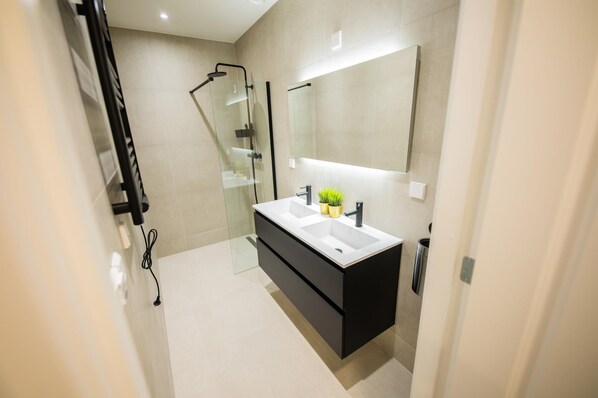A modern bathroom with a glass shower enclosure, a large mirror, and a black vanity with two sinks.
