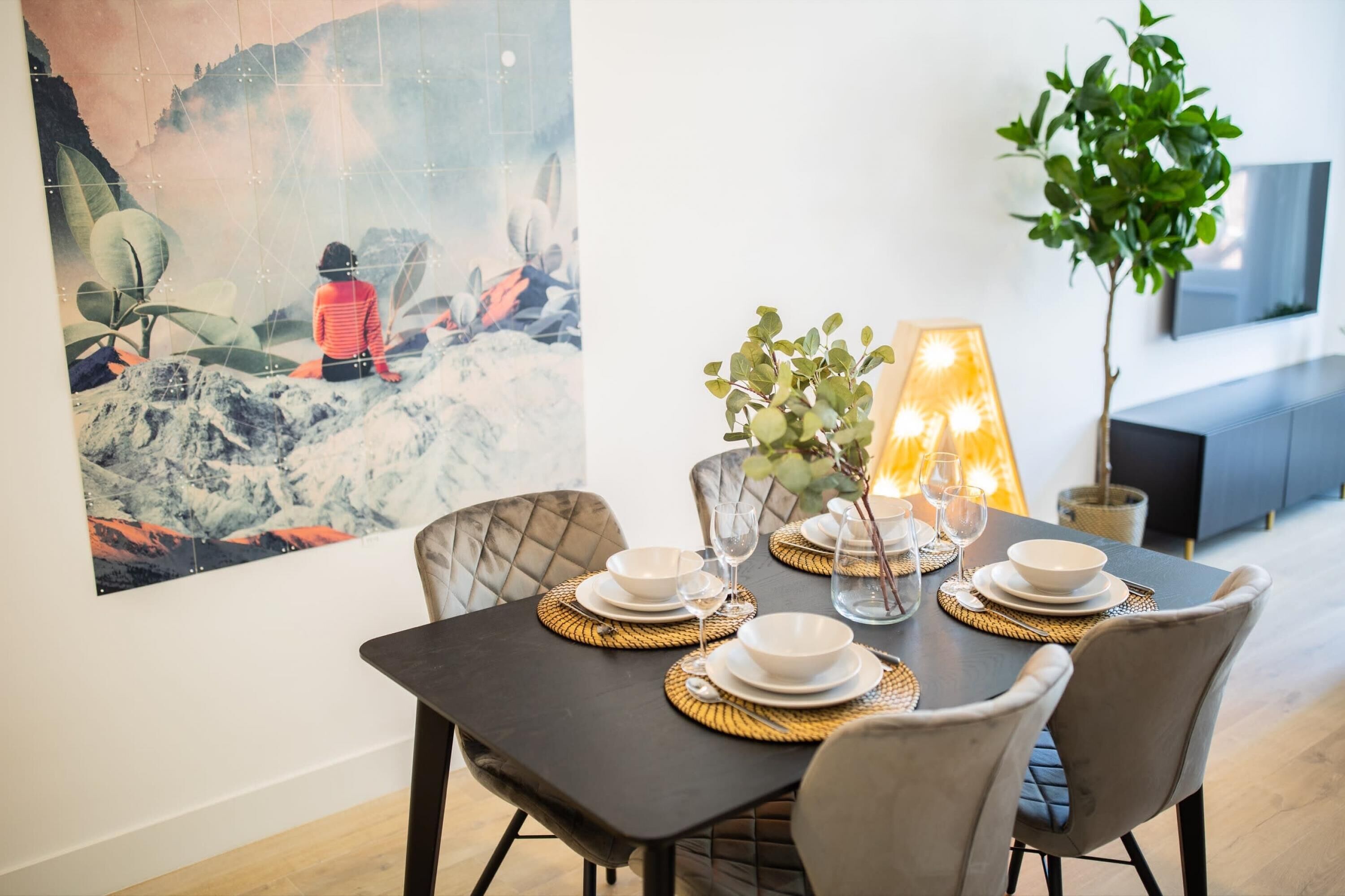 Une table à manger dressée avec des assiettes, des verres et un vase décoré de verdure.