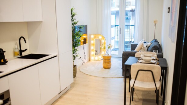Een moderne keuken met witte kasten, een zwarte kraan, en een eethoek met een tafel en stoelen.