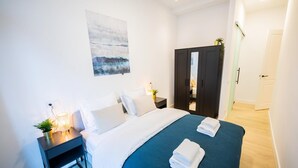Een moderne hotelkamer met een opgemaakt bed, een nachtkastje met een lamp, een kledingkast en een schilderij aan de muur.
