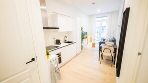 Een moderne keuken met witte kasten, een zwart aanrecht en een spoelbak. Er is een eethoek met een tafel en stoelen, en een plant op de achtergrond.