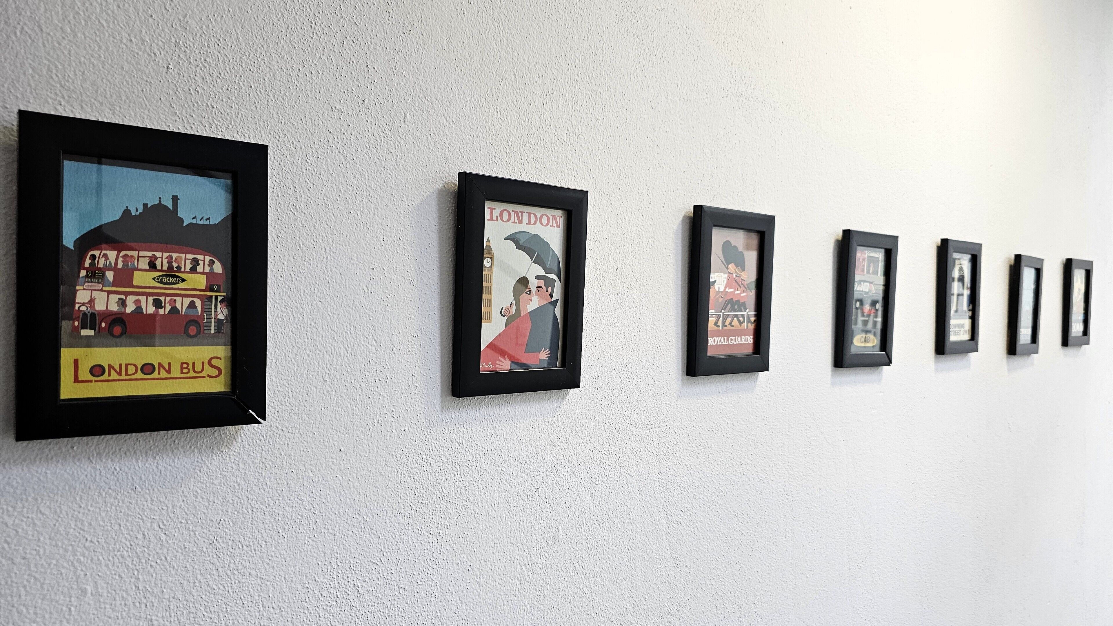 A wall with multiple framed pictures, including a double-decker bus and a couple under an umbrella.