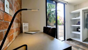 A modern room with a brick wall, a desk with a lamp, a sliding glass door to a balcony, and a white shelving unit. - R05 Habitación Equipada STV WIFI Parking (Atizapan de Zaragoza)