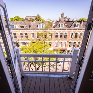 A balcony with a view of traditional European buildings, a wooden floor, and a white railing.