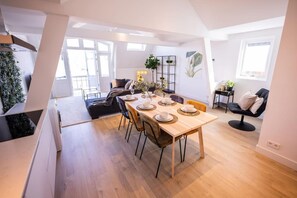 A modern dining area with a wooden table set for four, surrounded by chairs. A staircase leads to an upper level, and a plant is visible in the background. - Nb304/306 3BR Serviced Apartments (Rotterdam)