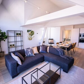 A modern living room with a sectional sofa, a glass coffee table, and a dining area with a table and chairs. - Nb304/306 3BR Serviced Apartments (Rotterdam)