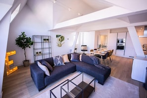 A modern living room with a sectional sofa, a dining area, and a kitchen. - Nb304/306 3BR Serviced Apartments (Rotterdam)