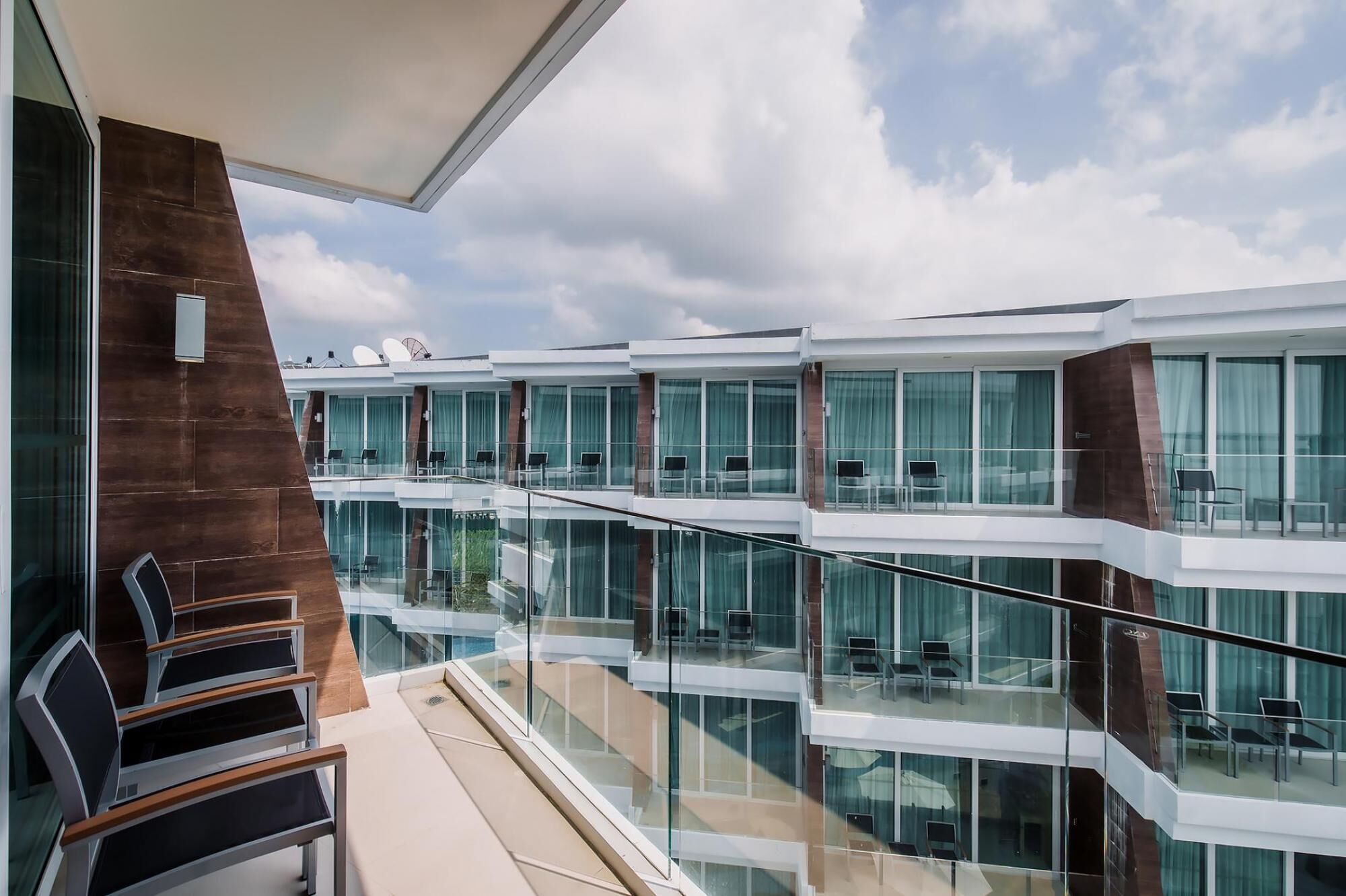 A modern hotel with multiple balconies, glass railings, and a clear sky view.