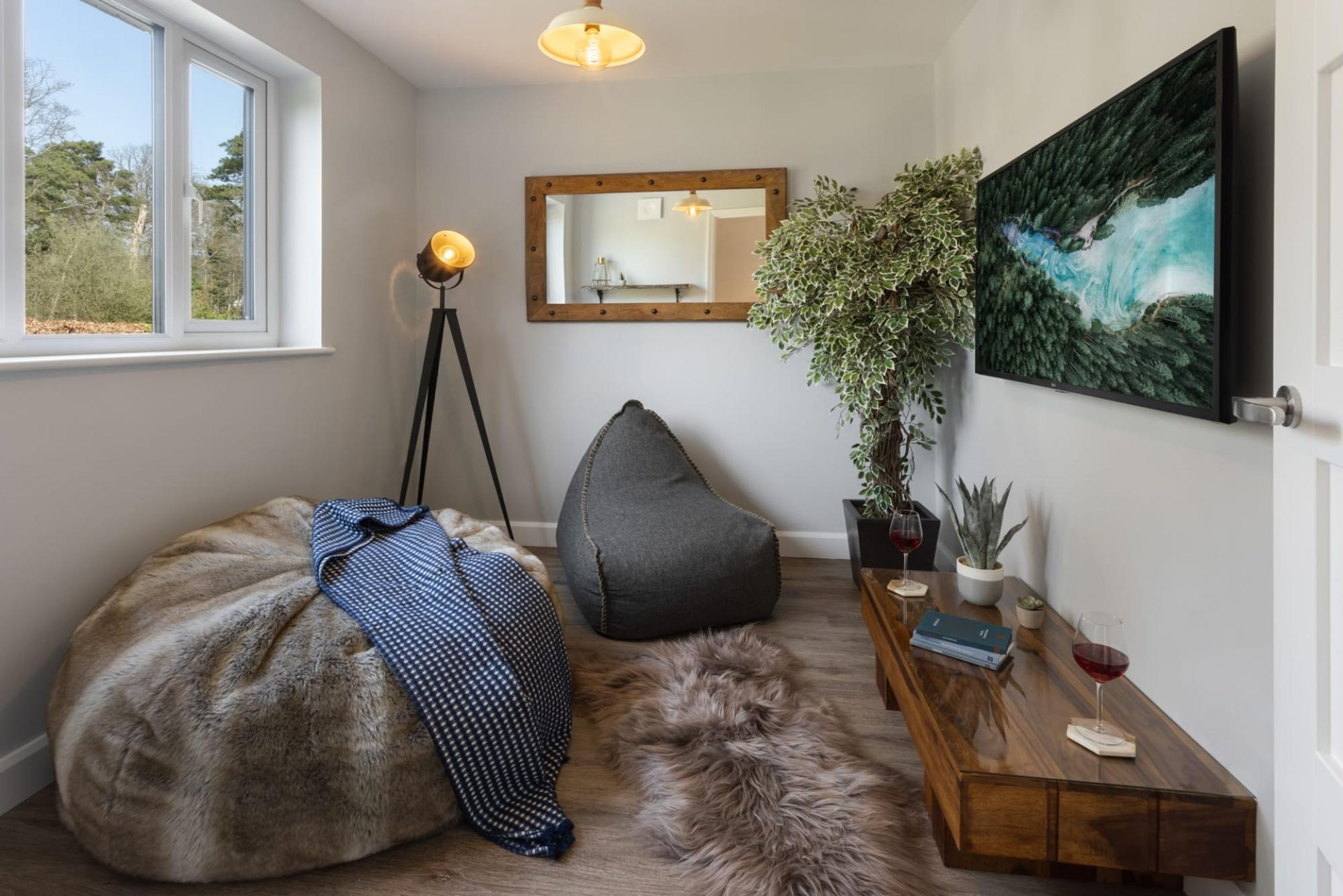 Una habitación acogedora con un sillón de grandes dimensiones, una mesita de madera con una copa de vino, un espejo y un cuadro en la pared.