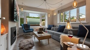 A modern living room with a sofa, a coffee table, a blue chair, and a fireplace. - Woodlands Family Retreat - Windermere Lakedistrict (Windermere)