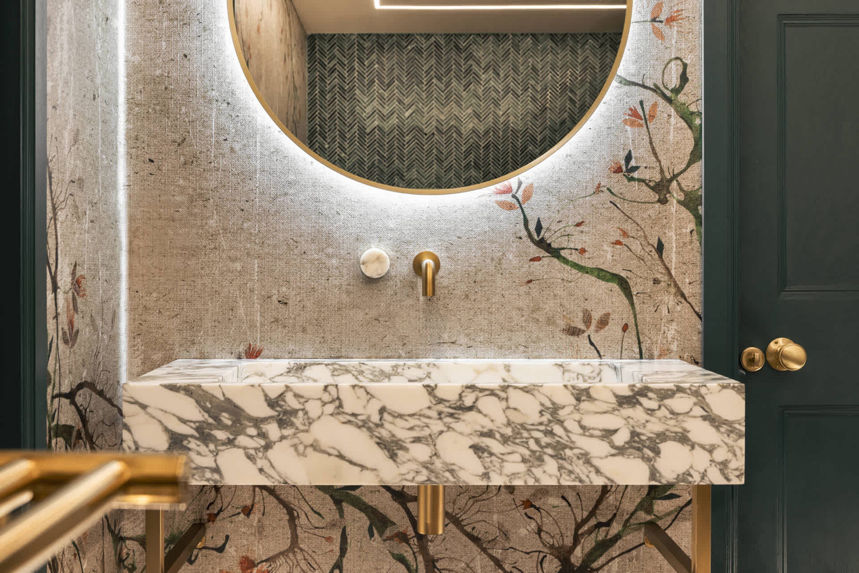 A bathroom with a marble sink, a round mirror, and a herringbone-patterned wall.