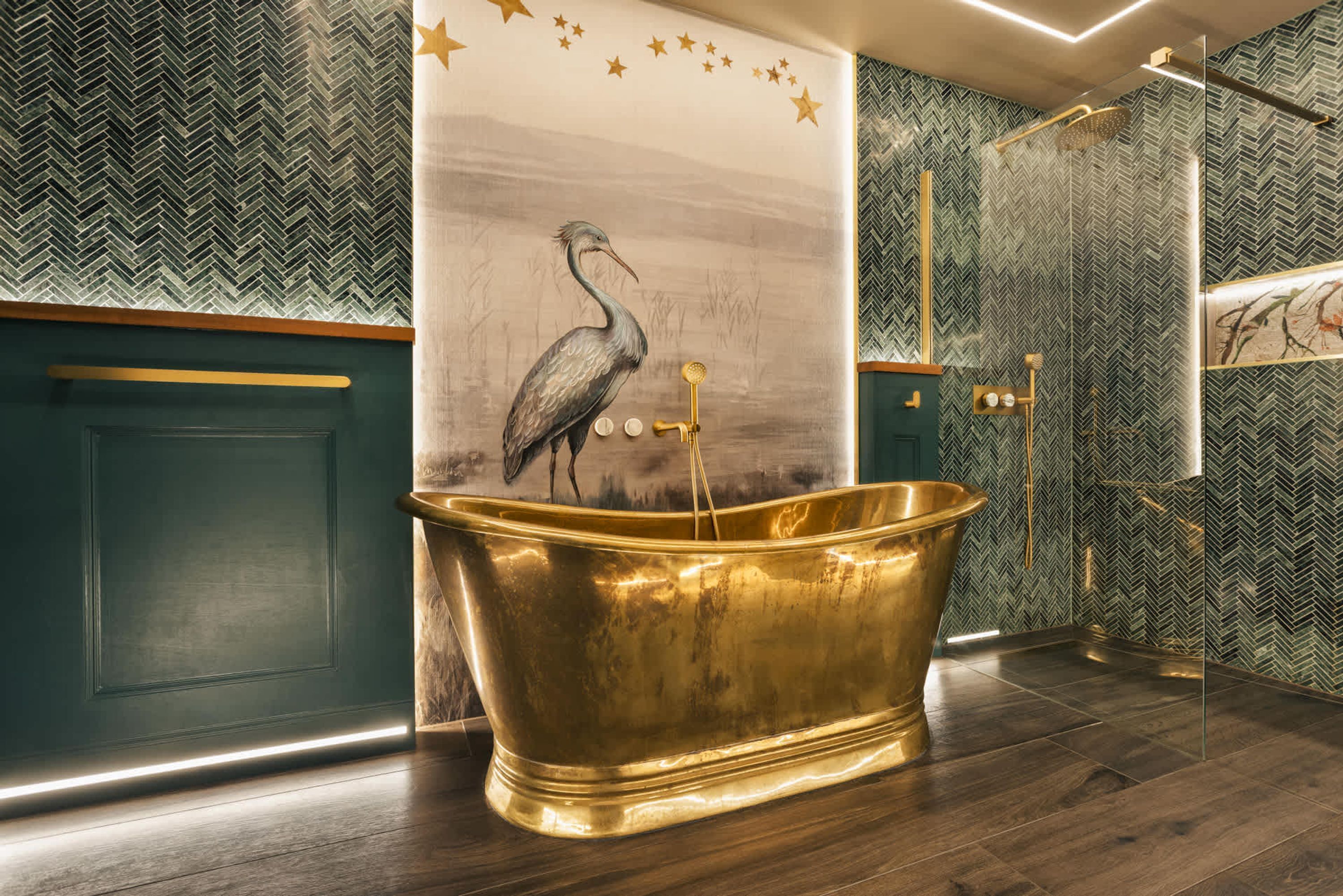 A bathroom with a large golden bathtub, a wall mural of a bird, and a shower area with a herringbone-patterned wall.