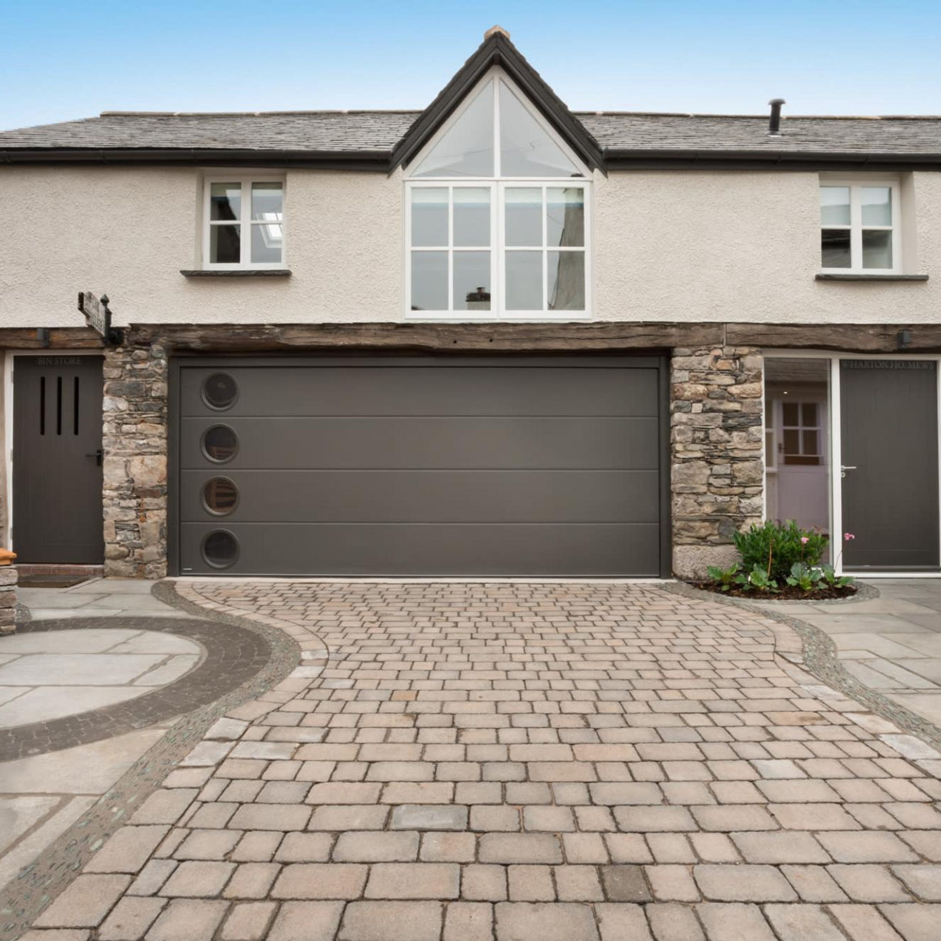 A two-story house with a garage, stone facade, and a paved driveway.