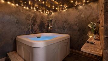 Un jacuzzi con un banco de madera, un estante con una copa y una botella de vino, y luces colgantes en el techo.