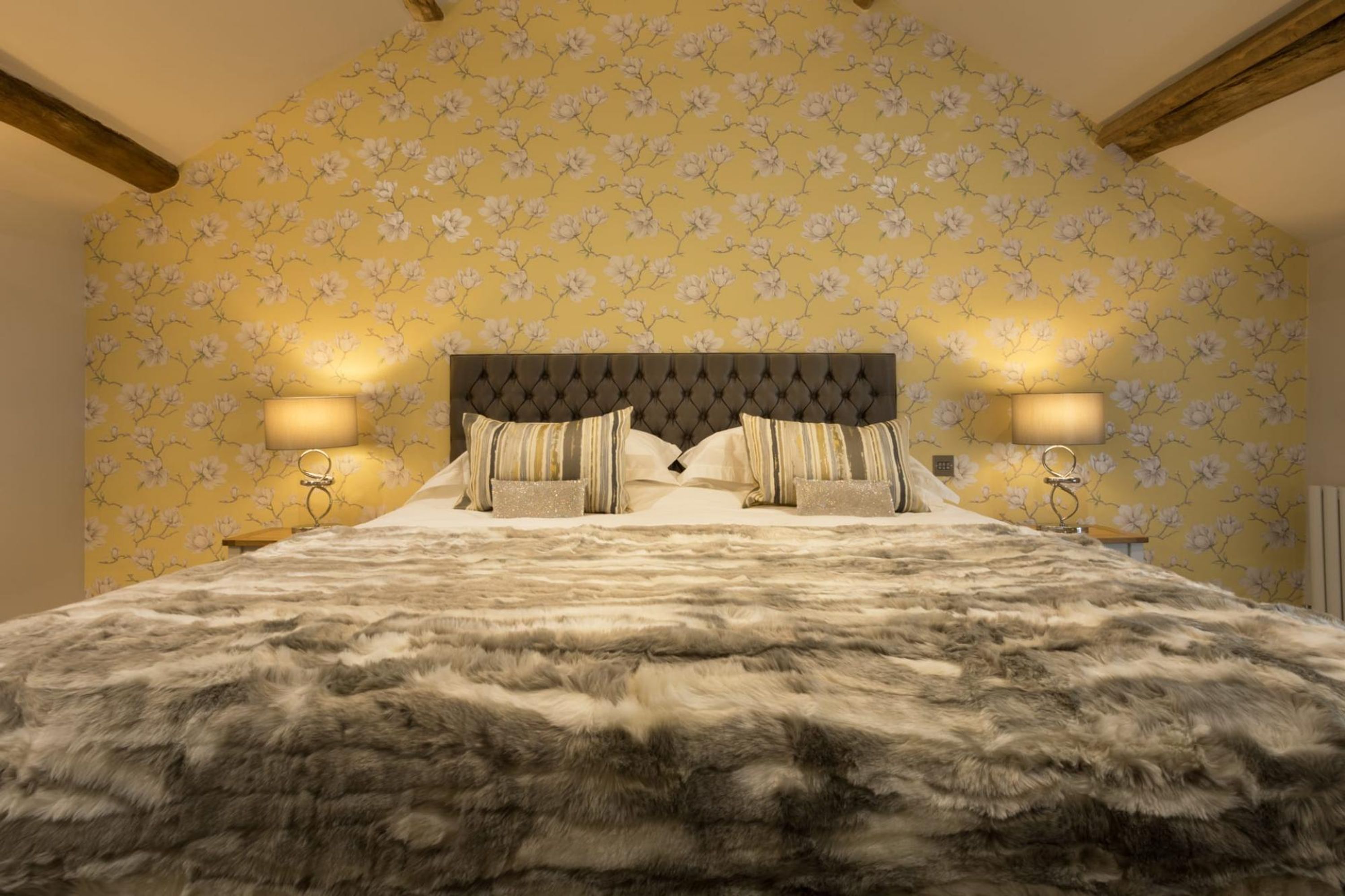 A bedroom with a large bed, floral wallpaper, and two bedside lamps.