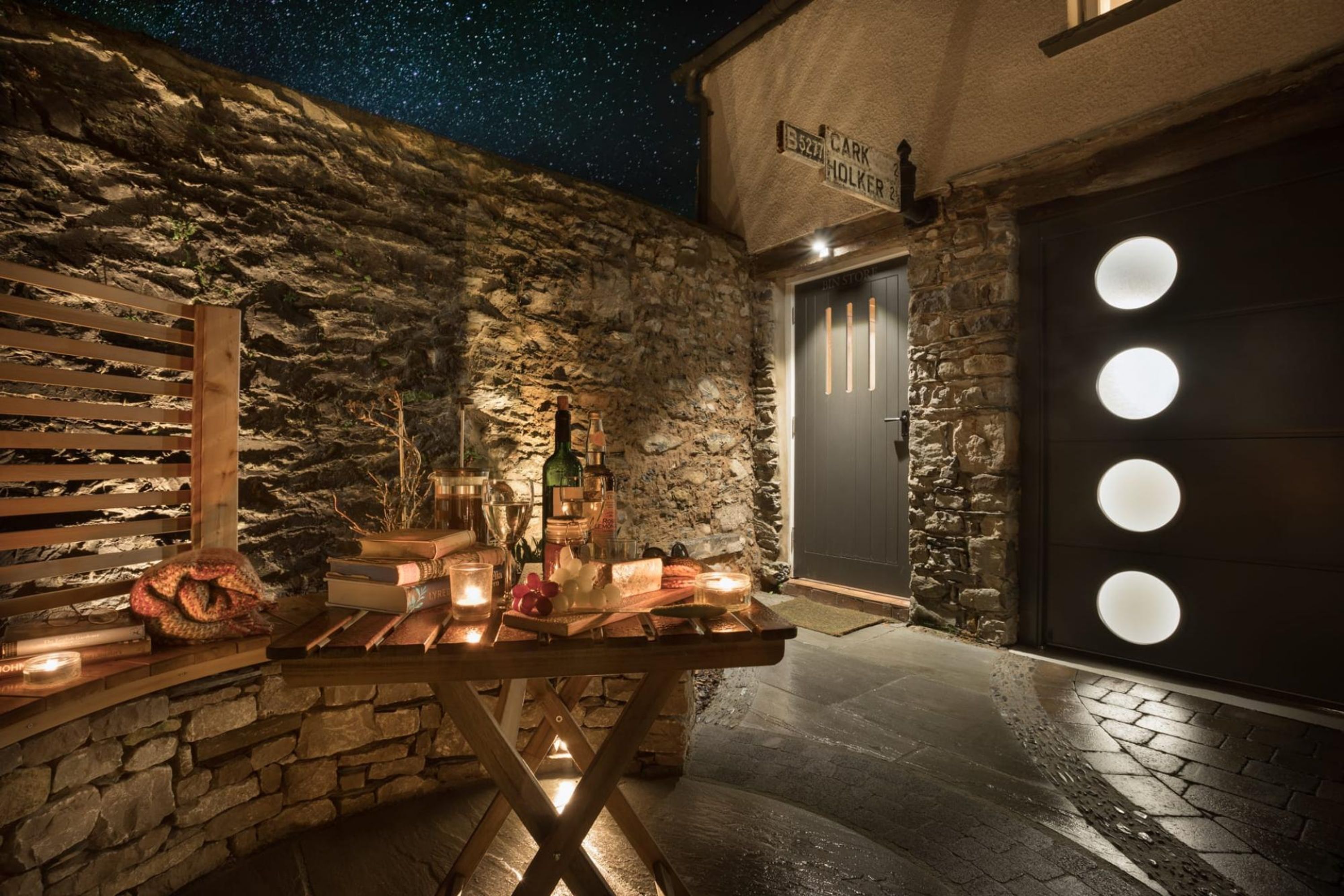 A stone wall with a wooden bench and a table set with candles and bottles.