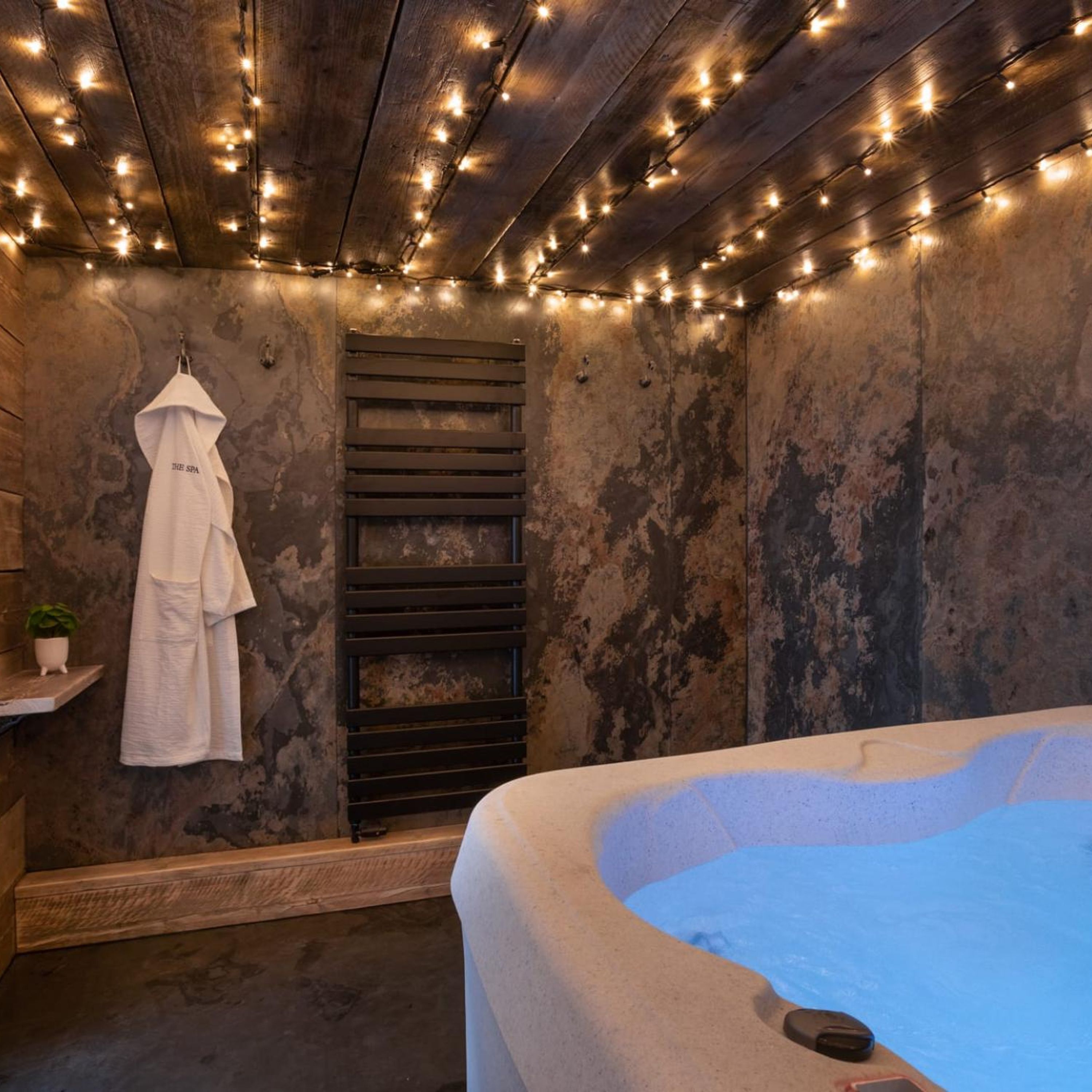 A spa room with a bathtub, a towel rack with a robe, and string lights on the ceiling.