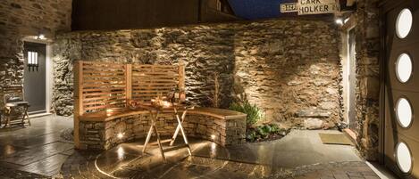 A stone-walled outdoor area with a wooden bench, a small table with candles, and a sign indicating 'CARK HOLKER'.