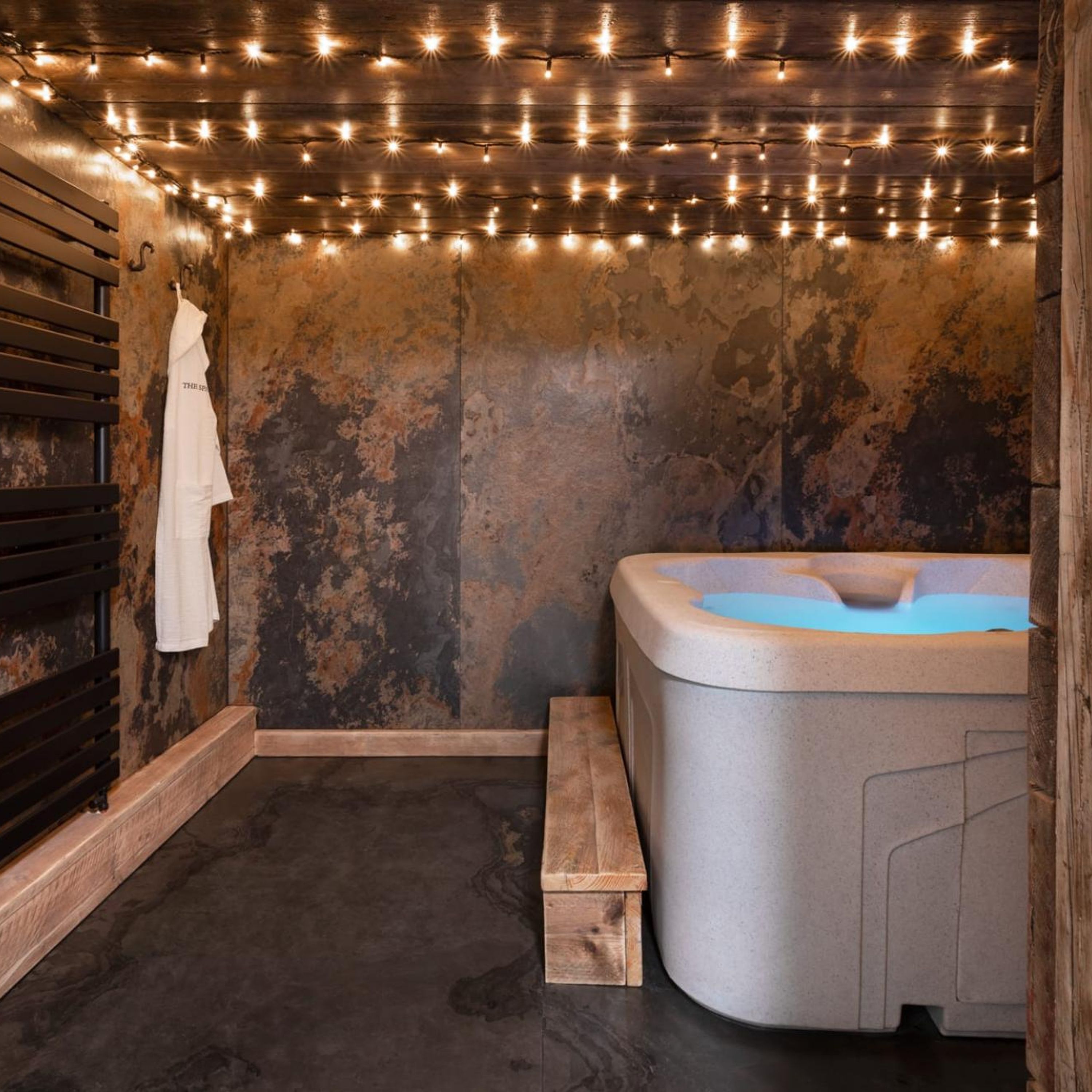 A spa room with a wooden bench, a hot tub, and string lights on the ceiling.
