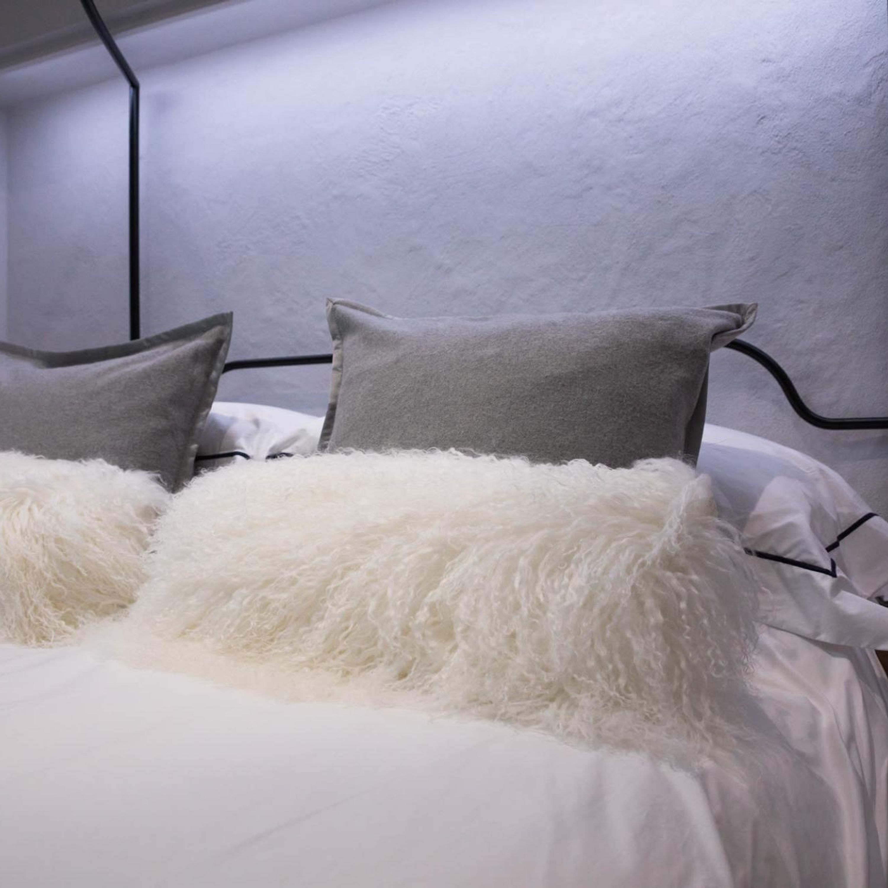 A bed with white and grey bedding, including fluffy white pillows and grey pillows.