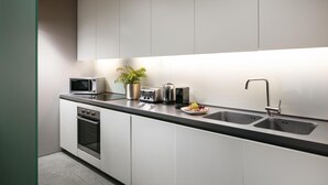 A modern kitchen with white cabinets, a black countertop, a microwave, a toaster, a sink, and a potted plant. - Two-bedroom Apartment at Royal William Yard (Plymouth)
