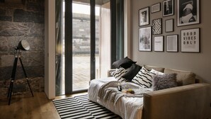 A modern living room with a large sliding glass door leading to an outdoor area, a stone wall, a tripod lamp, and a sofa with patterned cushions. - Two-bedroom Apartment at Royal William Yard (Plymouth)