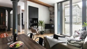 A modern living room with a dining area, large windows, and a stone wall. - Two-bedroom Apartment at Royal William Yard (Plymouth)