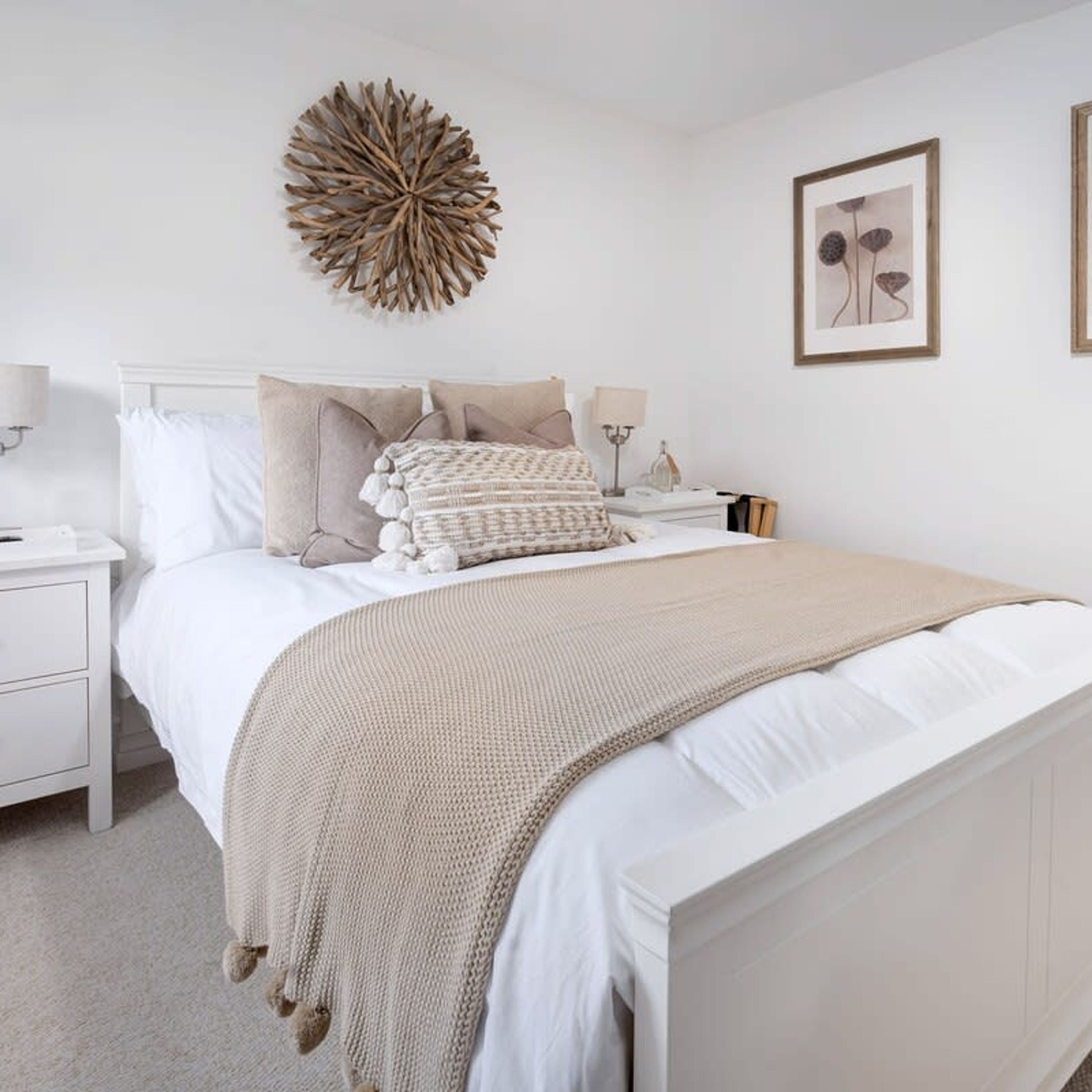Een keurig opgemaakt slaapkamer met een groot bed, witte beddengoed, een decoratief wandobject en ingelijste kunstwerken.