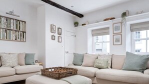 Una sala de estar con un sofá color beige, un tapete estampado y una estantería.
