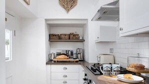 Una cocina compacta con armarios blancos, una decoración en forma de corazón en la pared, una encimera con hogaza de pan, una cafetera y un plato con un sándwich.