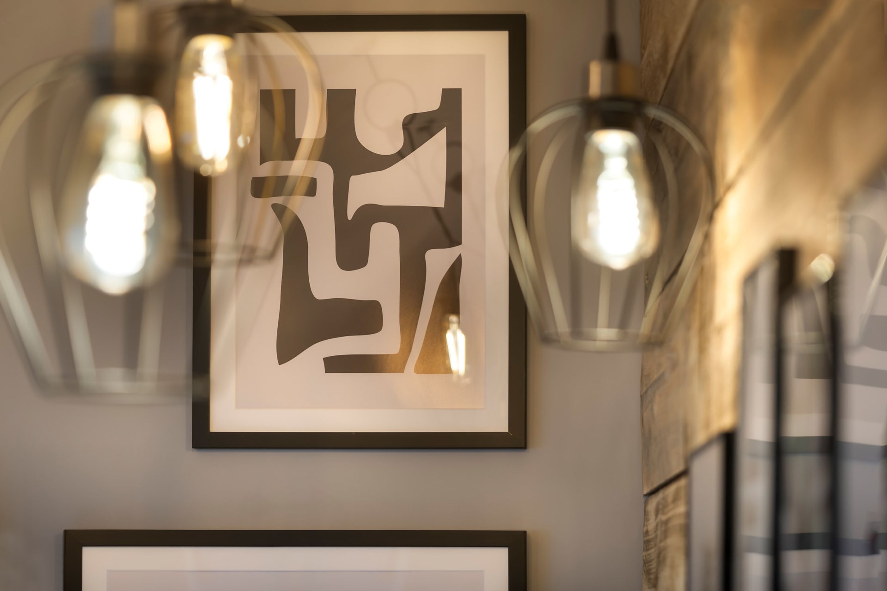 A framed abstract artwork on a wall with hanging light fixtures.