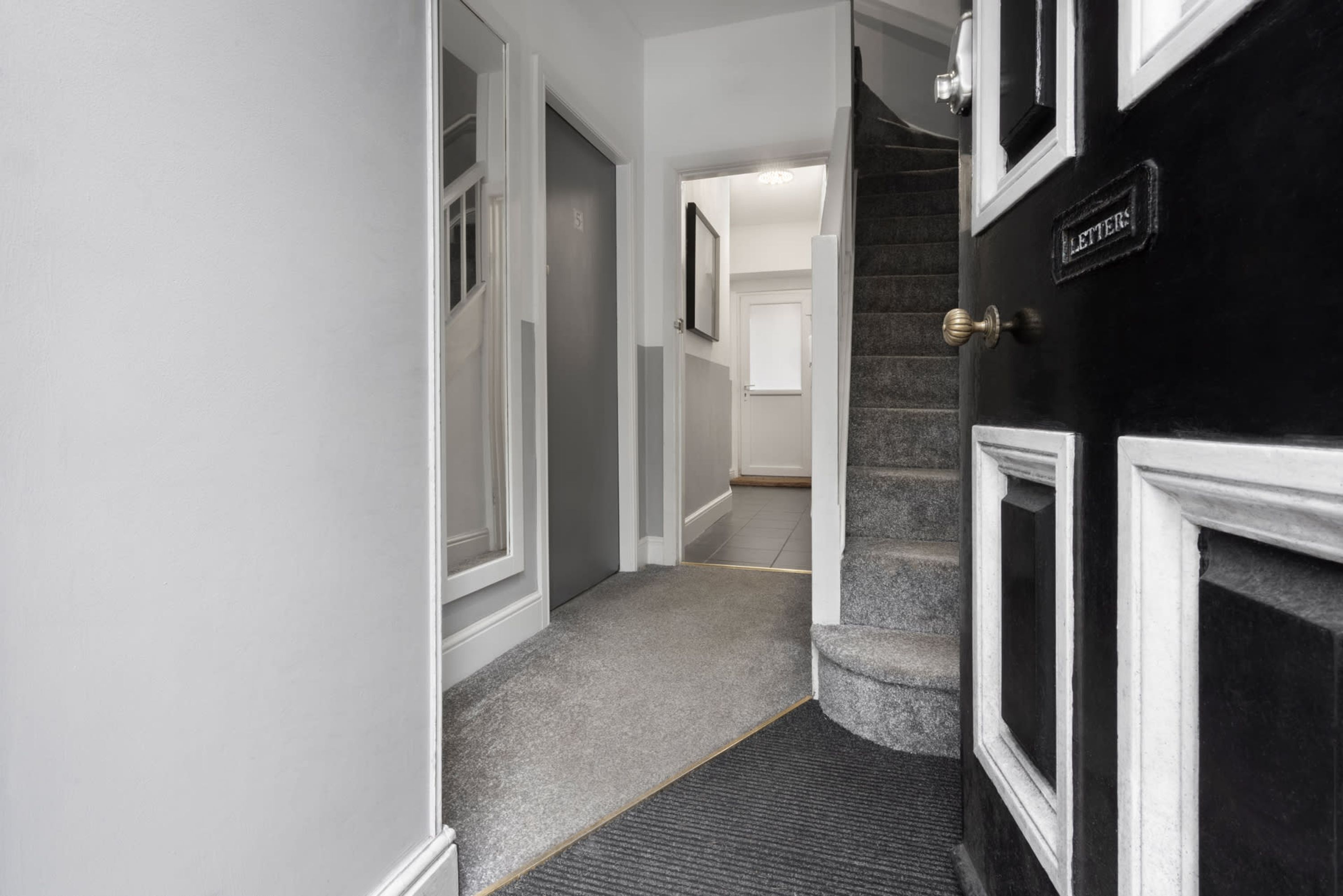 Un pasillo con suelo alfombrado, una puerta con la leyenda 'LETTERS' y una escalera que conduce a otra habitación.
