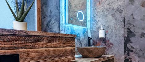 A bathroom with a wooden vanity, a sink with a stone basin, and a potted aloe vera plant.