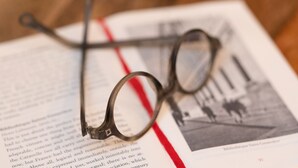 Une paire de lunettes posée sur un livre ouvert, marqué par un marque-page rouge.