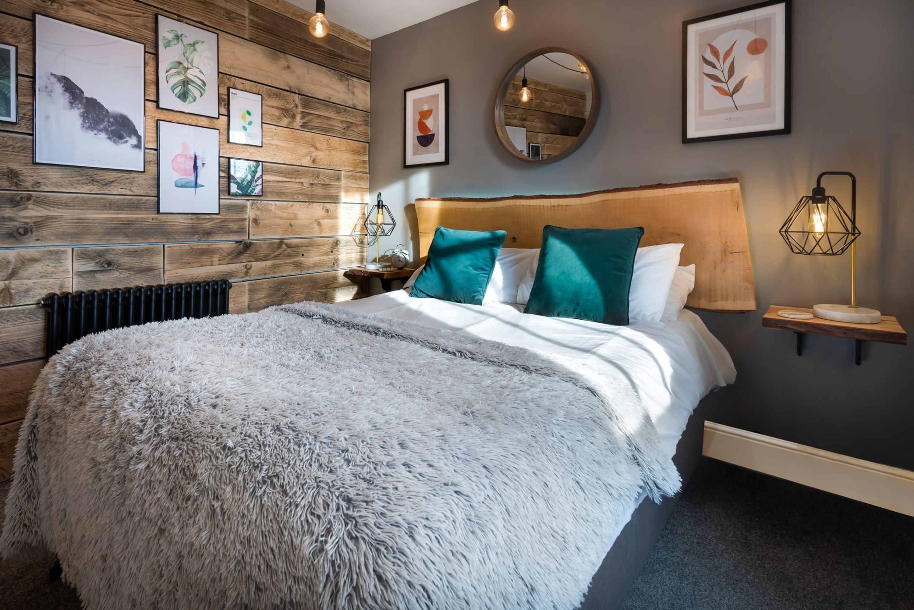 A modern bedroom with a wooden headboard, a fluffy white bedspread, teal pillows, and framed artwork on the wall.