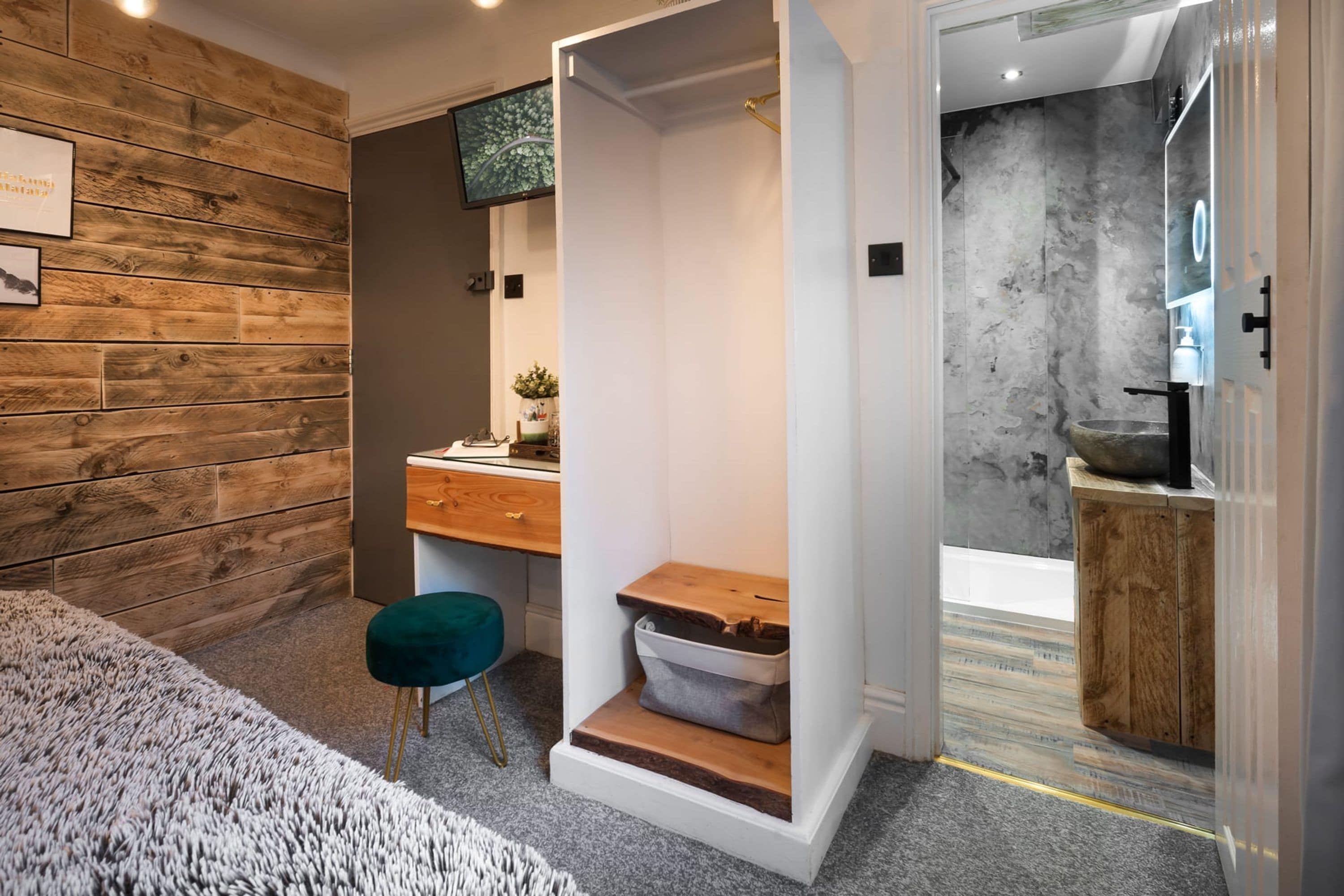Une chambre moderne avec un mur en bois, un bureau, une chaise et une salle de bain équipée d’une baignoire et d’un lavabo.