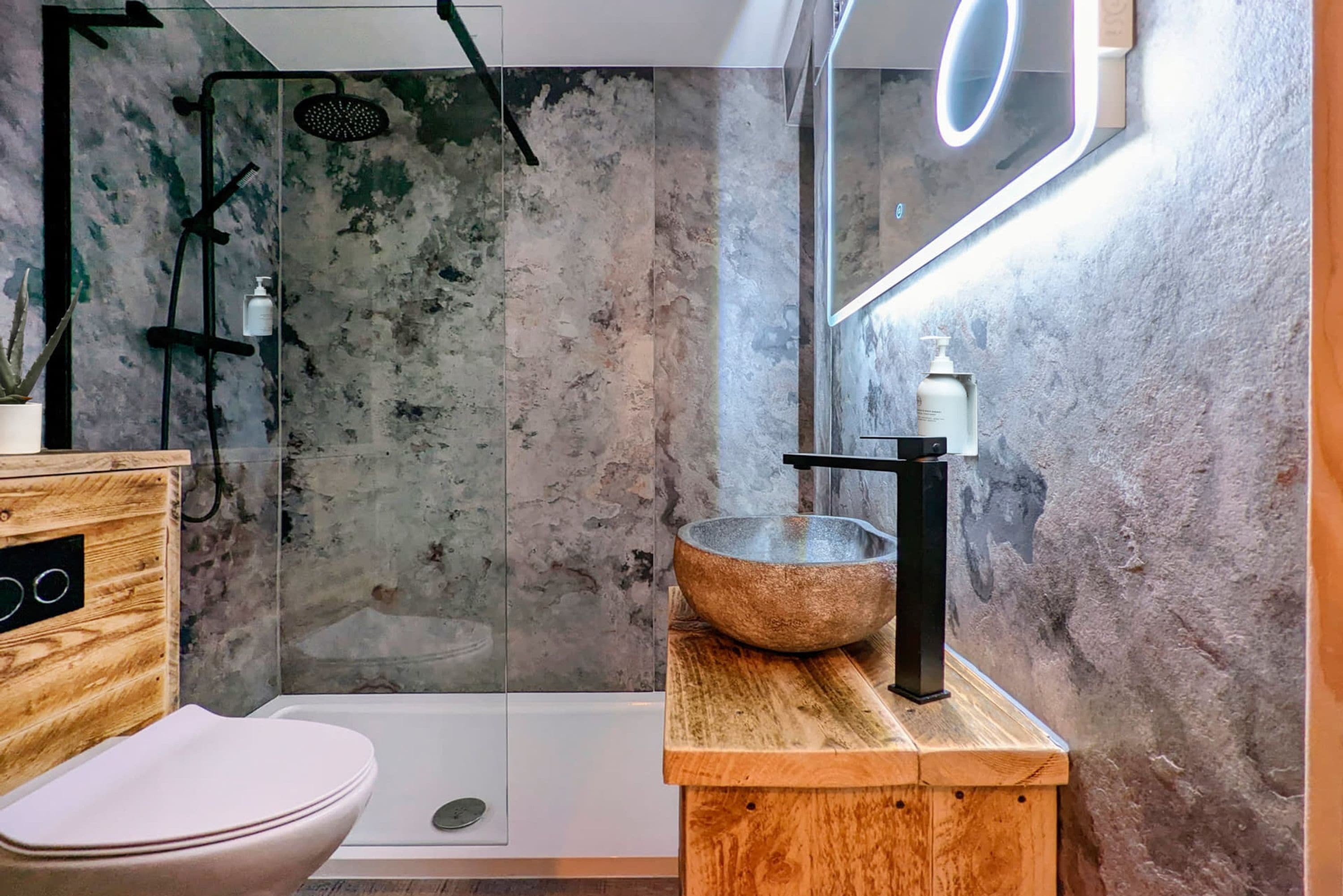 Un baño moderno con ducha de vidrio, tocador de madera con lavabo y un inodoro.