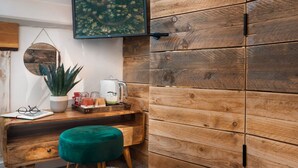 A cozy room with a wooden wall, a desk with a plant, a green ottoman, and a framed picture above the desk. - Windermere Central Hotel - Room 4 (Windermere)