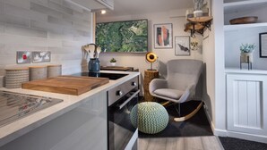A modern kitchen with a central island, built-in oven, and a grey armchair. - Eden Escape - Comfy Apartment Quiet Neighbourhood (Kendal)