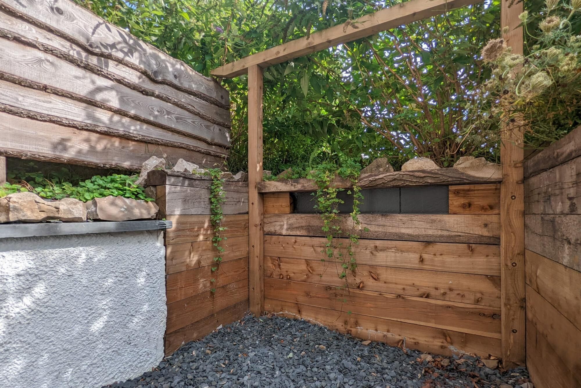 A wooden garden structure with a stone wall and a wooden pergola.